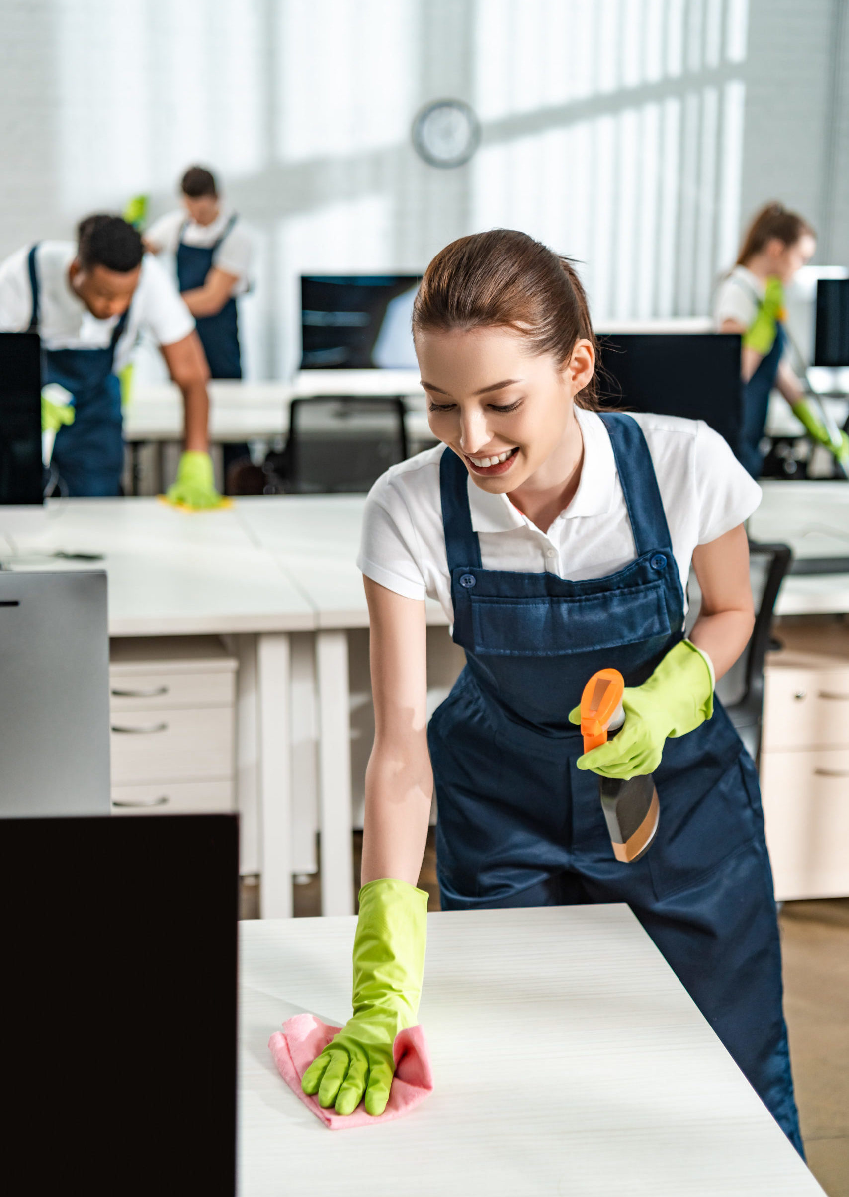 cheerful cleaner in overalls cleaning office desk with rag
